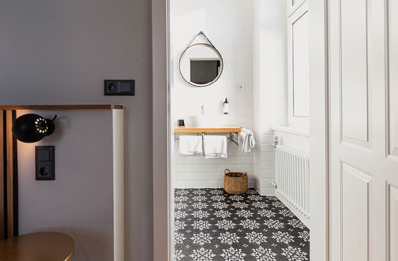 Dem geräumigen Bad mit beleuchtetem Spiegel verleihen ein großes Fenster und ein ästhetischer, schwarz-weiß gemusterter Fließenboden einen einladenden Charakter.